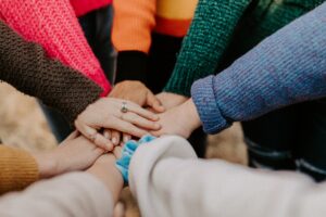 Verschillende handen die op elkaar samenkomen, ter symbolisering van het elkaar helpen. Dit artikel gaat over 5 manieren om mensen met een beperking te helpen.